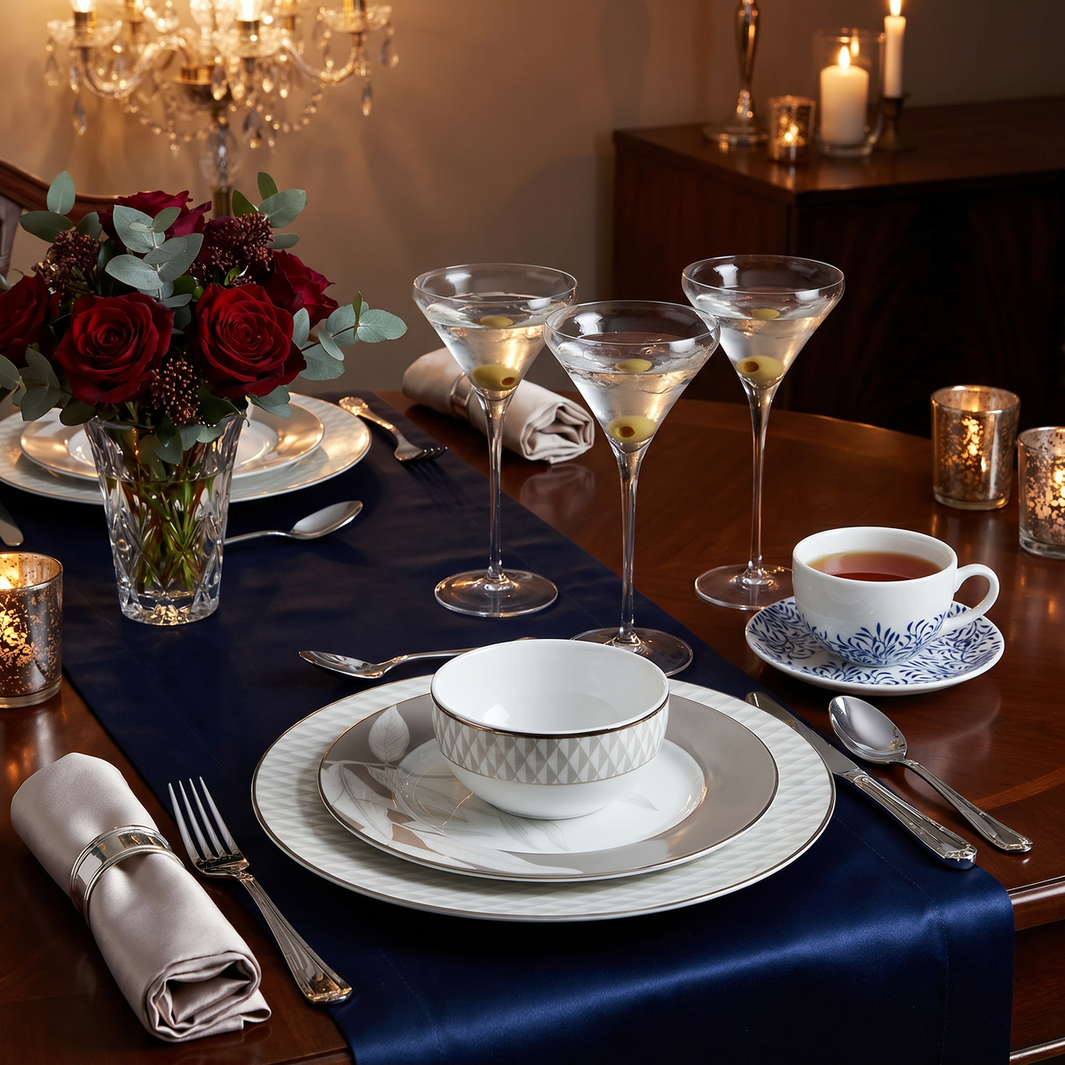 Premium white and silver porcelain dinner set with matching tea cups, crystal-style glassware, and elegant cutlery, styled with red roses and candles on a luxury dining table.